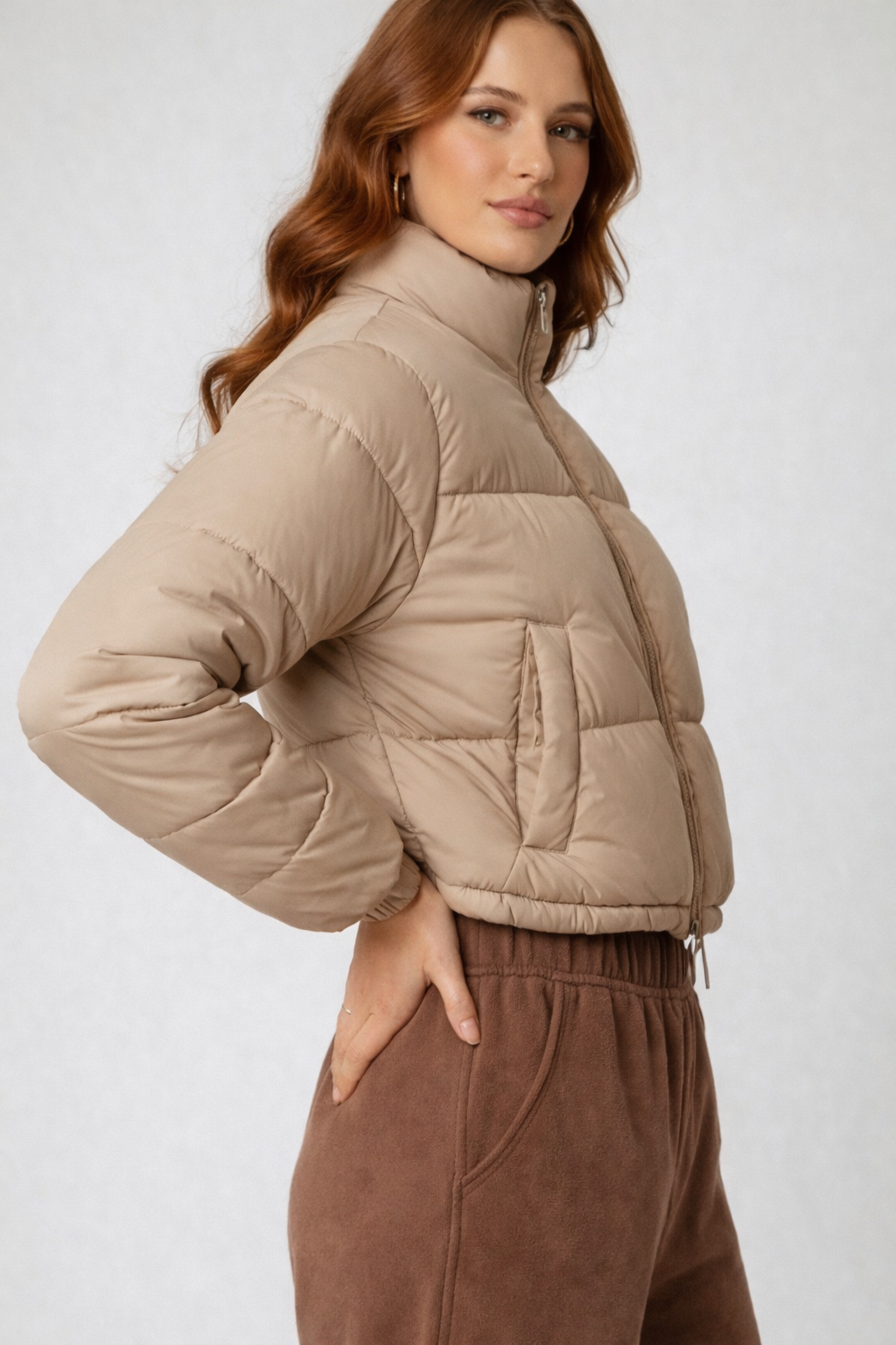 Woman wearing a beige puffer jacket and brown pants on a white background