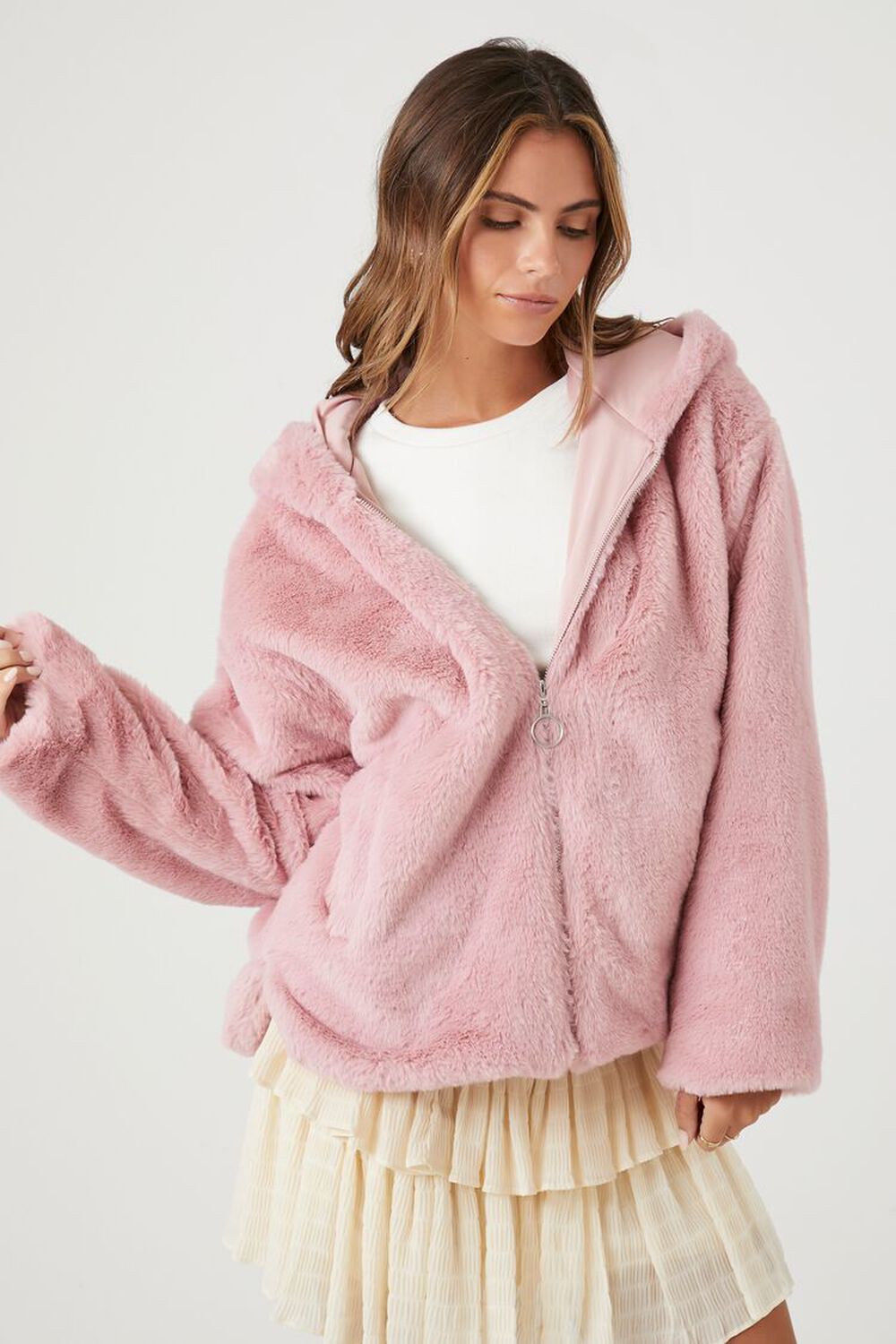 A woman wearing a Pale Mauve Forever 21 Plush Faux Fur Zip-Up Hoodie with a white sweater and a cream-colored skirt
